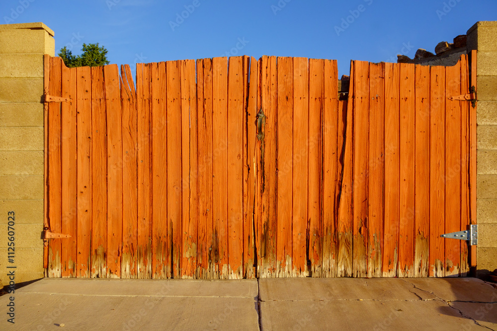 Fototapeta premium Driveway entrance gate with well weathered painted in red wooden planks and metal handle in between block columns
