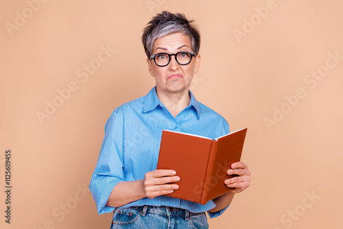 фотографія Elderly woman with a quirky expression holding a book against a beige background