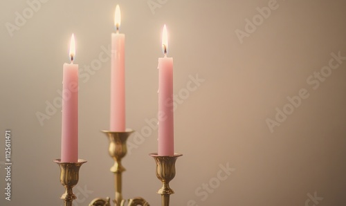 Three pink candles are lit and sitting on a gold candlestick photo