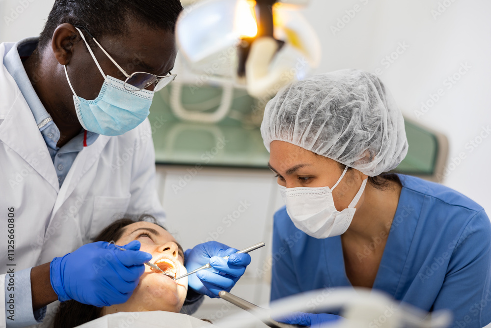 African-american man dentist and asian woman assistant doing tooth restoration for female patient.