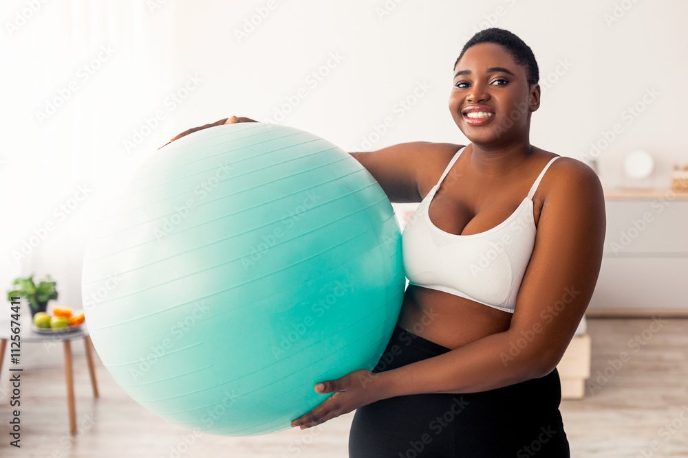 Portrait of plus size Afro lady in sportswear holding fitness ball after domestic training, indoors. Overweight black woman exercising at home, doing weight loss workout Portrait of plus size Afro lady in sportswear holding fitness ball after domestic training, indoors. Overweight black woman exercising at home, doing weight loss workout