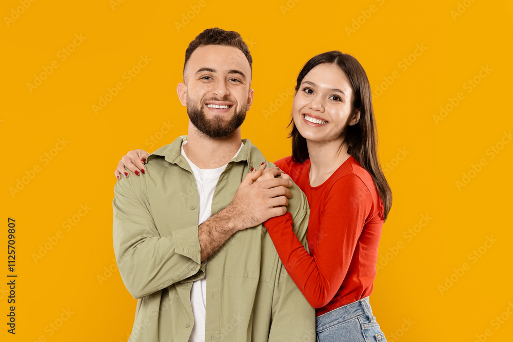 A happy couple stands closely together, smiling against a vibrant yellow background. Their affectionate poses convey love and joy, reflecting their youthful spirit and bond as spouses. A happy couple stands closely together, smiling against a vibrant yellow background. Their affectionate poses convey love and joy, reflecting their youthful spirit and bond as spouses.
