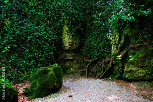 Curious view from the Pit of Monsters of Sentiero Li Vurgacci in Pioraco, spooky faces sculpted on the rock amidst dark greenery, musky boulders, roots of trees, in this Sibillini mountains' gorge photo