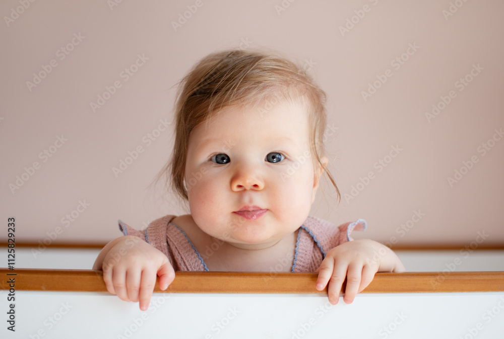 Portrait of a cute Caucasian baby girl 7 months old standing in a crib and looking at the camera. Copy space Portrait of a cute Caucasian baby girl 7 months old standing in a crib and looking at the camera. Copy space