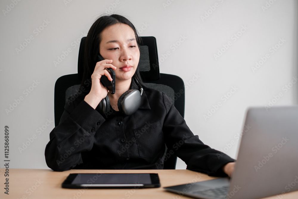 Professional woman multitasking with a laptop and smartphone in a contemporary office environment.