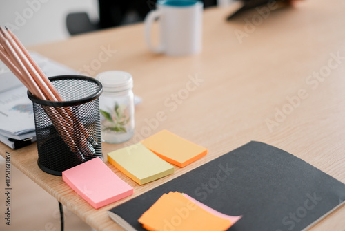 Photos A tidy office desk featuring colorful sticky notes, pencils in a holder, and a notebook, ideal for productivity and organization themes
