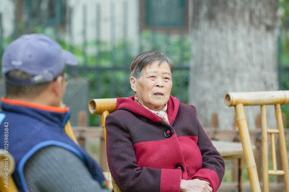 Obraz premium On a cold winter evening, a Chinese woman in her 70s and her grandson, a man in his 30s, sit on a bamboo bench in Qingpu District, Shanghai, China and look at the scenery together.