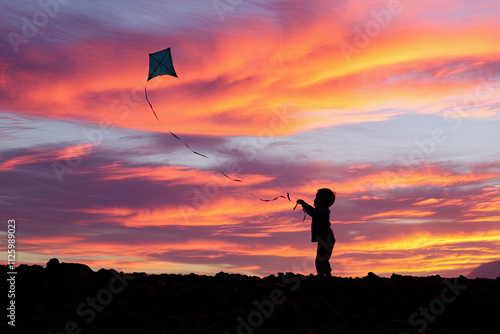 Child playing with a kite, silhouetted against a vibrant sunset sky photo