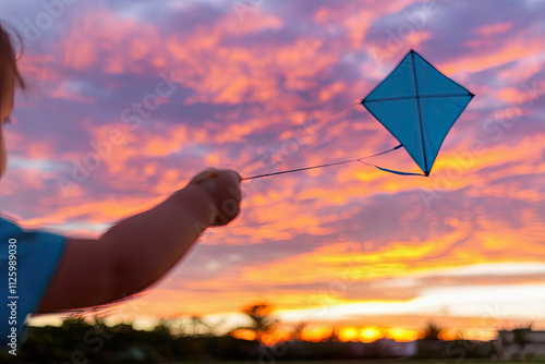 Child playing with a kite, silhouetted against a vibrant sunset sky photo