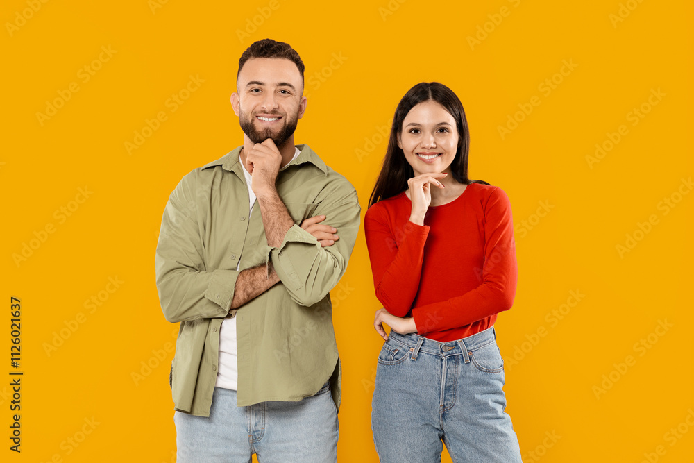 A young couple stands side by side in a vibrant yellow setting. They share playful expressions while resting their chins on their hands, showcasing their affection and joy. A young couple stands side by side in a vibrant yellow setting. They share playful expressions while resting their chins on their hands, showcasing their affection and joy.