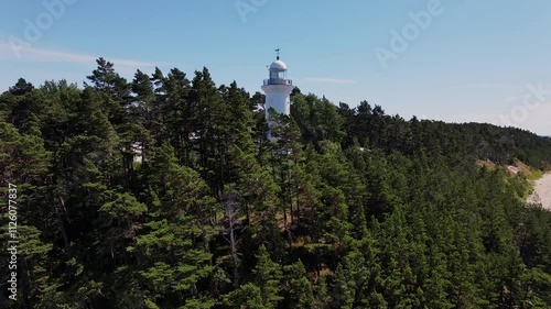 Drone ascending over Uzava lighthouse, showing the white tower amidst green forest photo