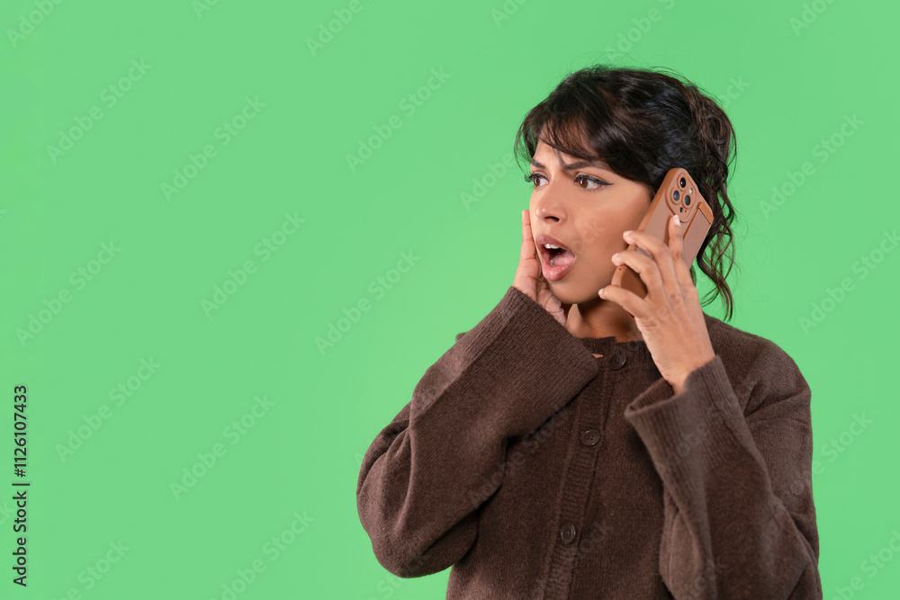 Woman reacting in surprise while speaking on a smartphone against a vibrant green background Woman reacting in surprise while speaking on a smartphone against a vibrant green background