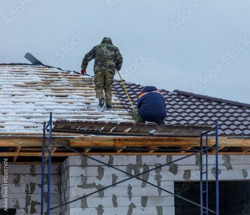 Wallpaper Mural A man in a camouflage jacket is on a roof, measuring the roof Torontodigital.ca