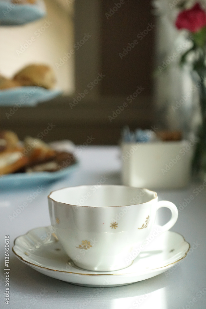 White porcelain teacup on table with pastries in background White porcelain teacup on table with pastries in background