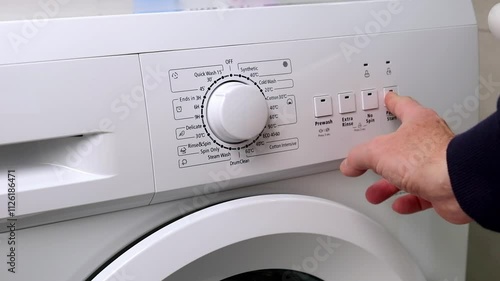 A man's hand turn circle selector for choosing the washing mode on the panel of the washing machine.