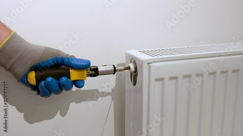 A plumber uses a special screwdriver to bleed air, draining water and air from a radiator in an apartment. Air bleed valve in a heating radiator.