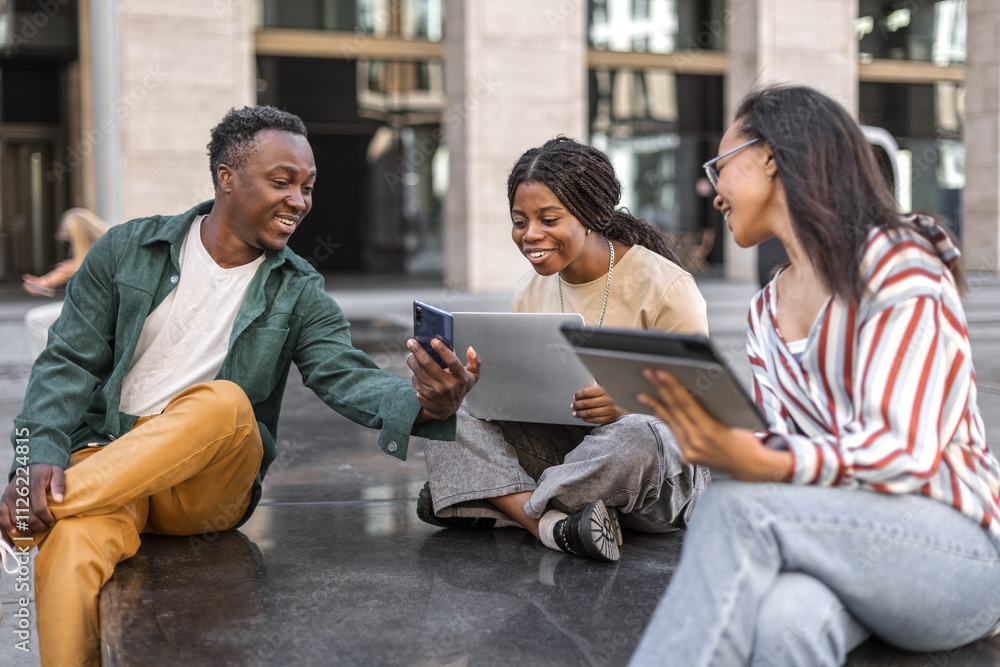 Cheerful young people sitting together chatting and using gadgets Cheerful young people sitting together chatting and using gadgets