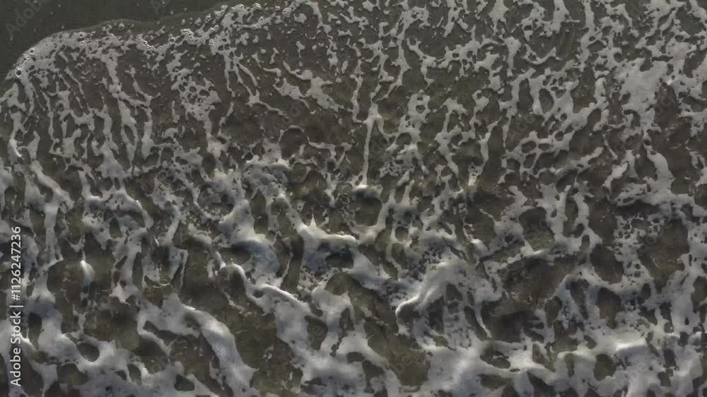 Aerial top down drone shot captures the dynamic patterns of seafoam, seawave along the shoreline. Ocean's movement and the textured coastline showcases nature's scenic beauty. Aerial top down drone shot captures the dynamic patterns of seafoam, seawave along the shoreline. Ocean's movement and the textured coastline showcases nature's scenic beauty.