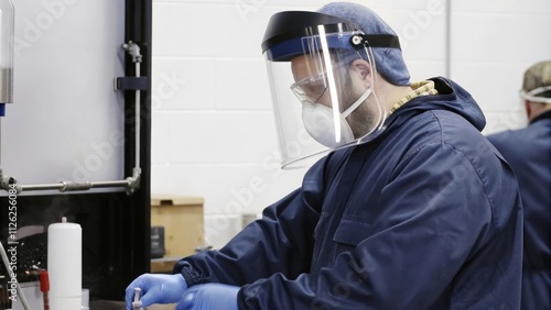 A technician performing a delicate operation under a laminar flow hood wearing a face shield and gloves ensuring a dustfree environment for semiconductor preparation.