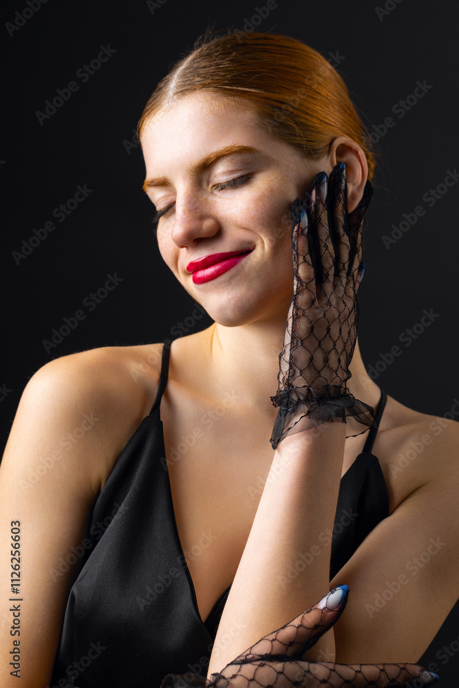 A young redhear girl with clean skin wearing black gloves. Beauty portrait of a woman on a black background in the studio.