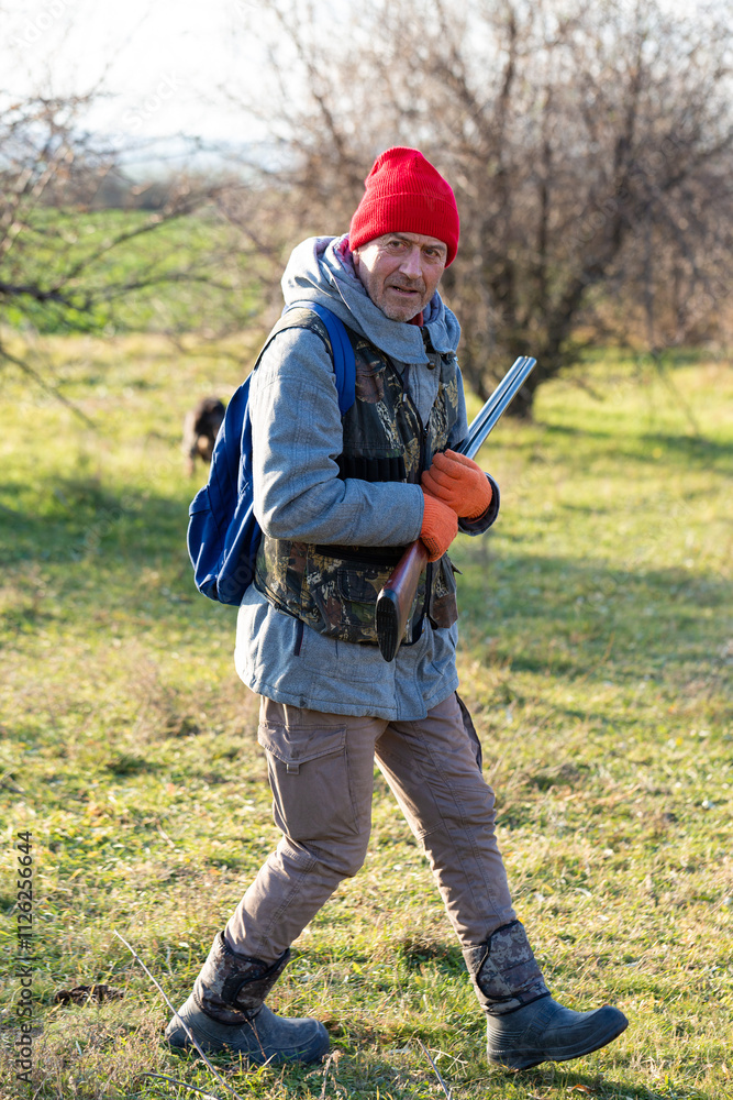 Mature hunter man holding a shotgun and walking through a field Mature hunter man holding a shotgun and walking through a field