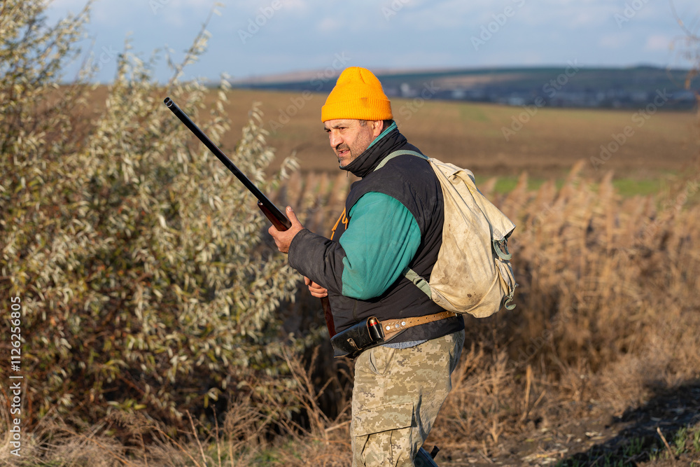Mature hunter man holding a shotgun and walking through a field Mature hunter man holding a shotgun and walking through a field