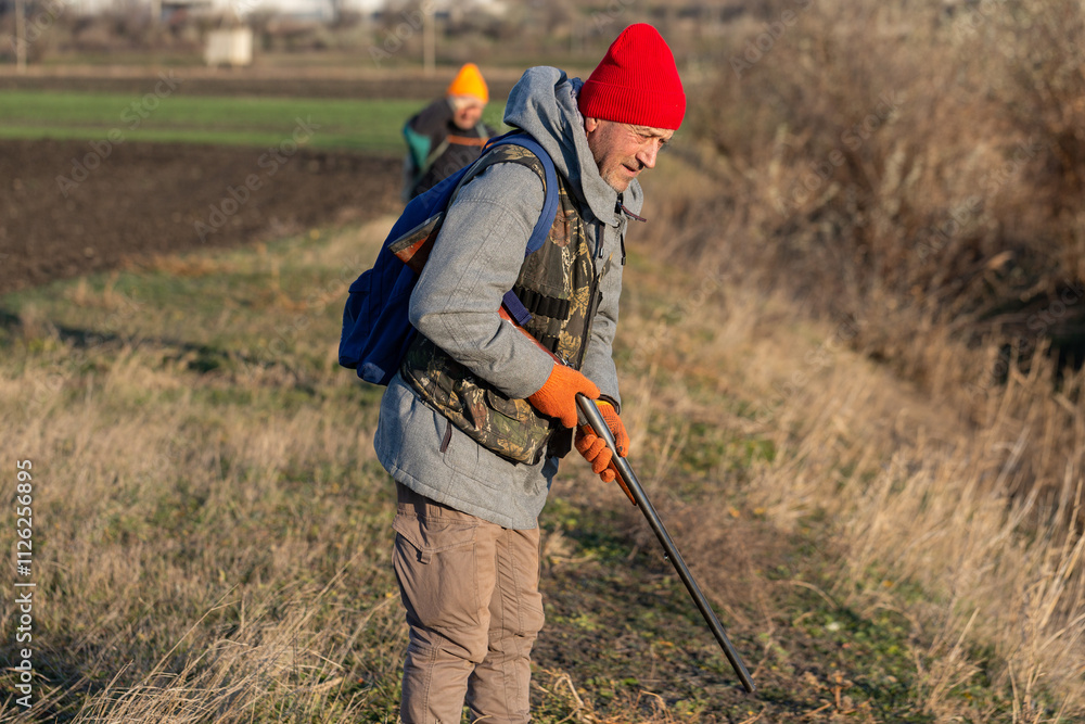 Mature hunter man holding a shotgun and walking through a field Mature hunter man holding a shotgun and walking through a field