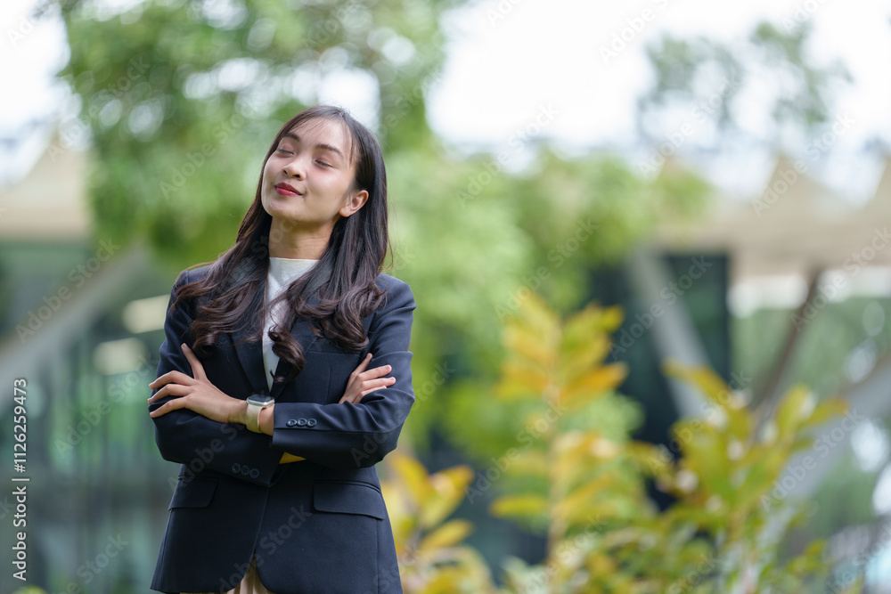 Happy Asian businesswoman standing with arms crossed and smiling relaxedly outside an office building during break time. Happy time working concept. Happy Asian businesswoman standing with arms crossed and smiling relaxedly outside an office building during break time. Happy time working concept.