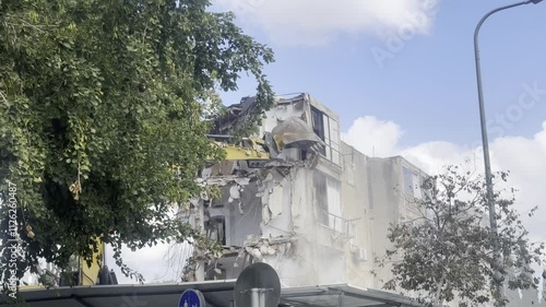 Excavator with large metal bucket breaks an old stone house. Demolition of obsolete building in city. Dangerous area is fenced off.