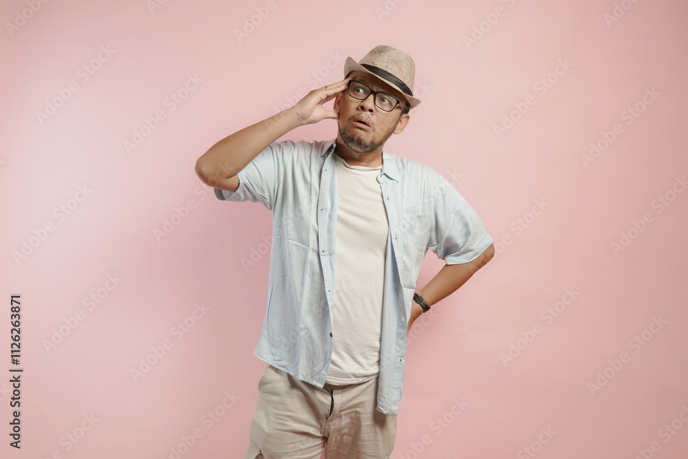 Thoughtful young Asian man wearing blue shirt and hat thinking of an idea with serious expression. Thoughtful young Asian man wearing blue shirt and hat thinking of an idea with serious expression.