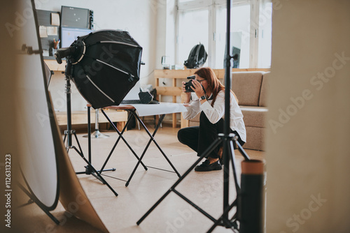 Female photographer taking photo of objects on background in photo studio with professional equipment