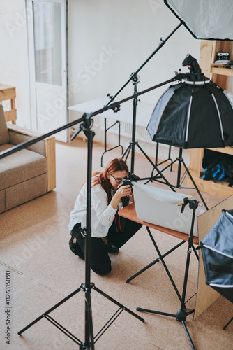 Female photographer taking photo of objects on background in photo studio with professional equipment