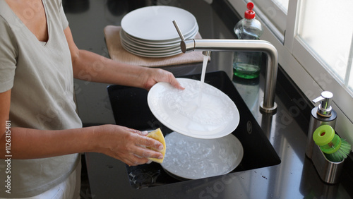 Bild auf Leinwand Woman washing and rinsing dishes by hand under a stream of water in the kitchen sink