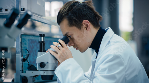 Portrait of a Young Graduate Student Working in a Laboratory, Using Advanced Microscope, Writing Down Research Data on a Computer. Multiethnic Biotechnology Specialist Using Modern Tools