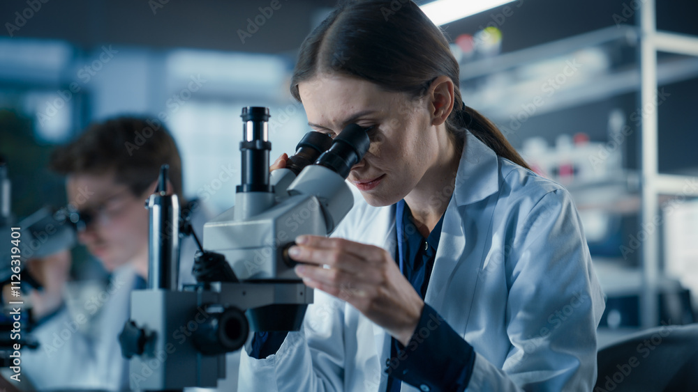 Focused Female Biotechnologist Studying Genetic Samples. Young Specialist Researching Data in Order to Develop New Medical Products. Group of Scientists Working in a Laboratory Focused Female Biotechnologist Studying Genetic Samples. Young Specialist Researching Data in Order to Develop New Medical Products. Group of Scientists Working in a Laboratory