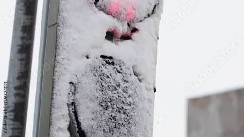 Red signal of a snowy, icy traffic light with a pedestrian sign, close-up. The concept of safety when crossing the road as a pedestrian winter. Slow motion photo