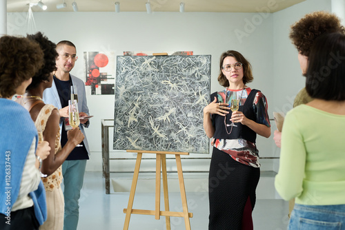 Canvas Print Young owner of art gallery holding glass of champagne and communicating to visit