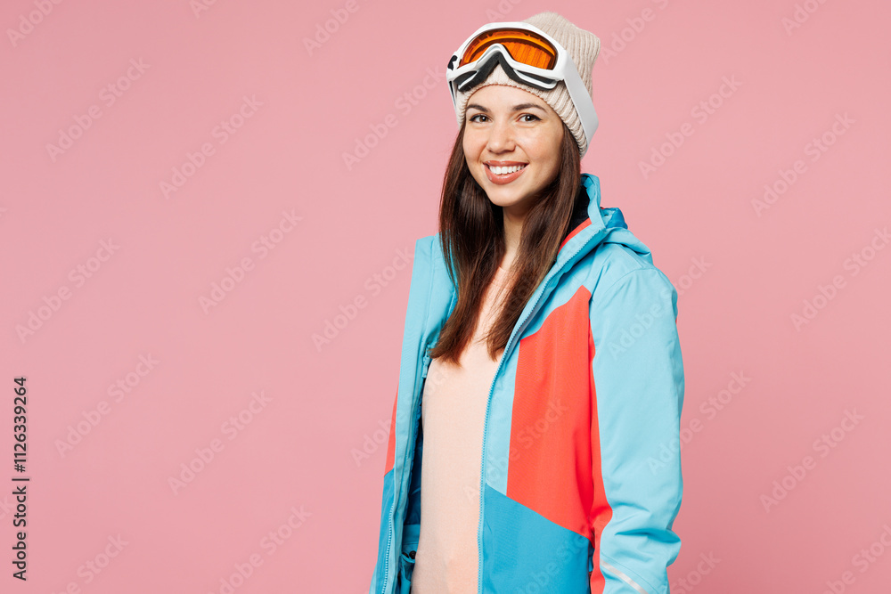 Side view skier young smiling happy woman wear warm blue padded jacket ski goggles mask spend extreme weekend winter season in mountains look camera isolated on plain pink background. Hobby concept. Side view skier young smiling happy woman wear warm blue padded jacket ski goggles mask spend extreme weekend winter season in mountains look camera isolated on plain pink background. Hobby concept.