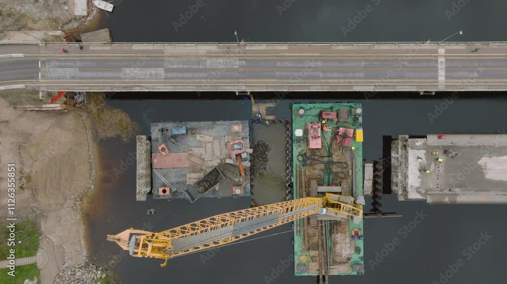 Aerial top down view of excavator machine building a bridge over Salaca river (Salacgriva city), dark autumn water, wide birdseye shot Aerial top down view of excavator machine building a bridge over Salaca river (Salacgriva city), dark autumn water, wide birdseye shot