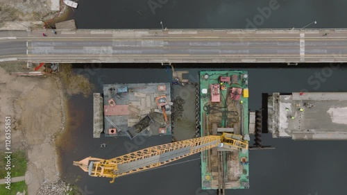 Aerial top down view of excavator machine building a bridge over Salaca river (Salacgriva city), dark autumn water, wide birdseye shot photo