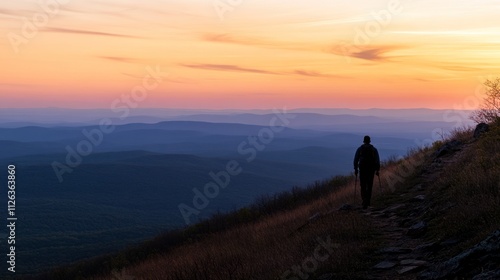 A solitary hiker walks along a scenic trail at sunset, surrounded by rolling hills and valleys.