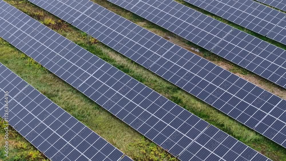 Drone of solar farm with rows of panels surrounded by green vegetation and grass Drone of solar farm with rows of panels surrounded by green vegetation and grass