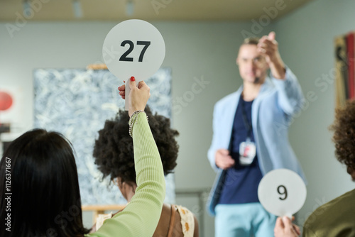 Картината върху платно Rear view of young brunette woman raising hand holding paddle with number twenty