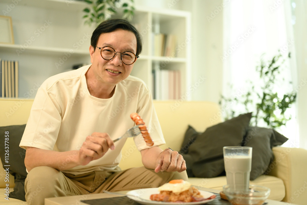 Happy middle aged man sitting on sofa, enjoying a plate of fried rice Happy middle aged man sitting on sofa, enjoying a plate of fried rice