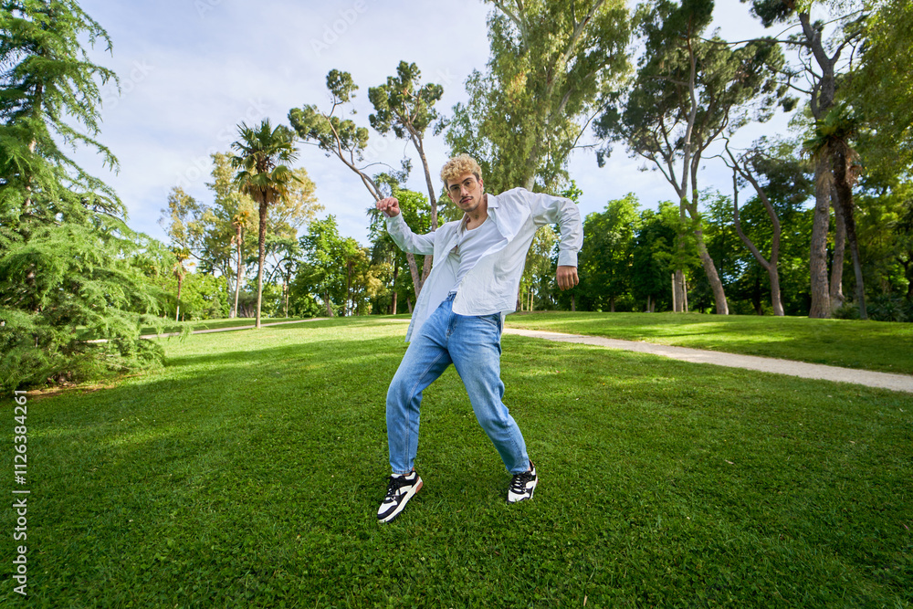 Latin man in white shirt and blue jeans dancing on a park lawn Latin man in white shirt and blue jeans dancing on a park lawn