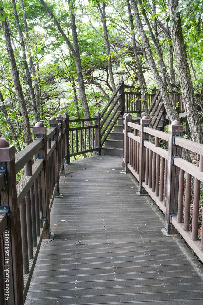 A wooden walkway with a wooden pavilion in the middle. The pavilion has a yellow sign on it. The walkway is surrounded by trees and has a peaceful, A wooden walkway with a wooden pavilion in the middle. The pavilion has a yellow sign on it. The walkway is surrounded by trees and has a peaceful,