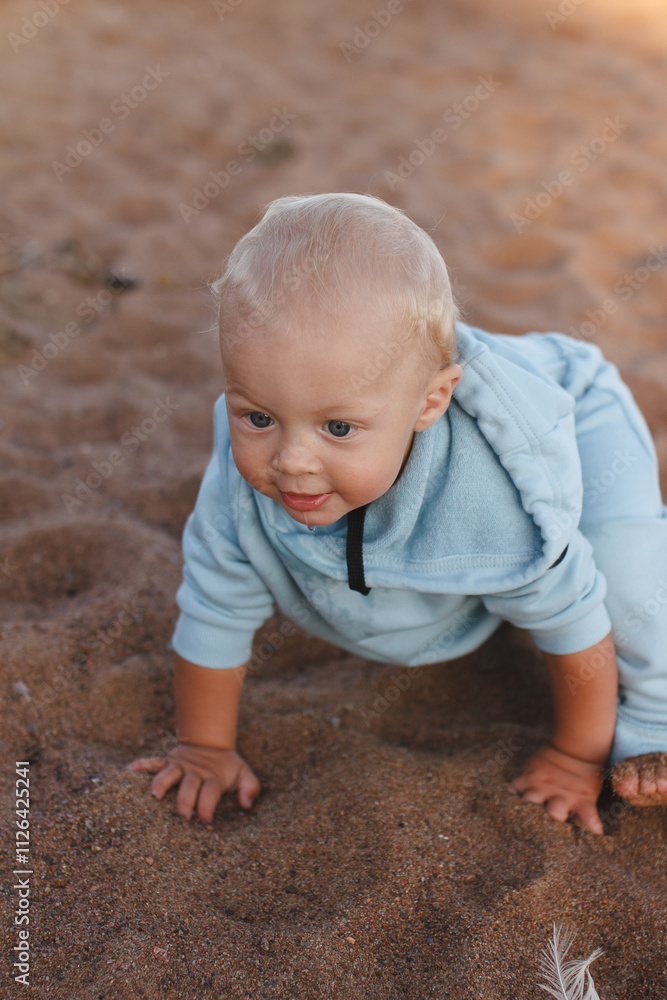 Happy toddler in blue hoodie crawls along beach on sunny day Happy toddler in blue hoodie crawls along beach on sunny day