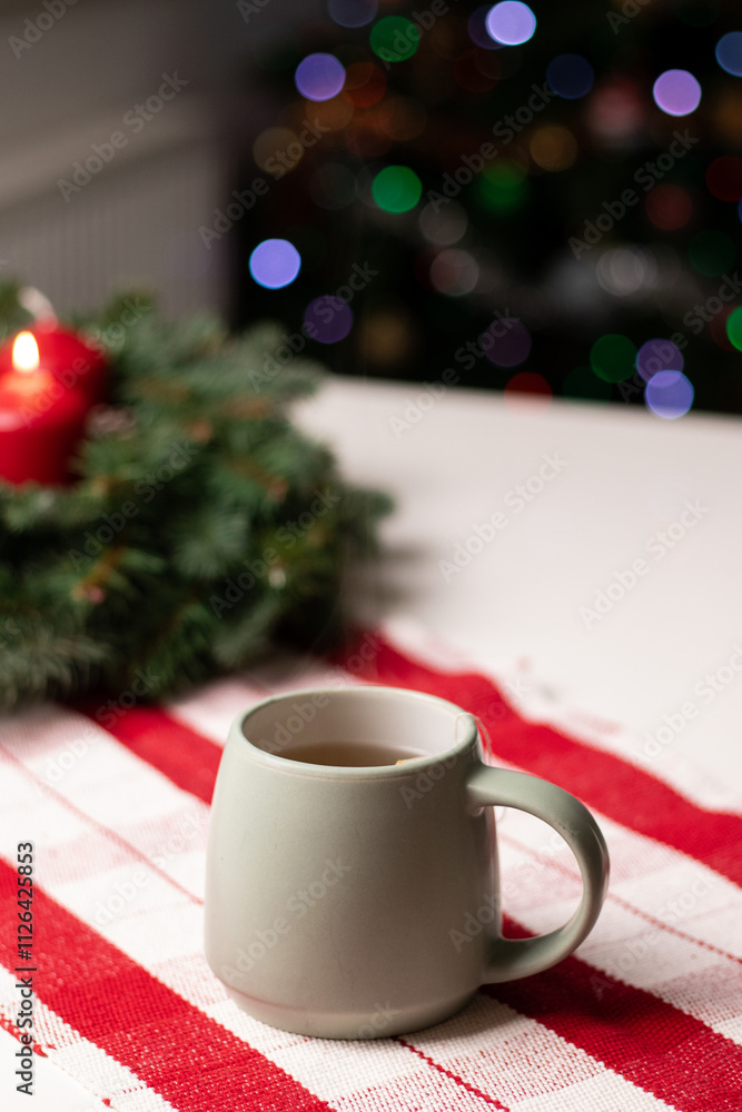 A cup with hot drink on white table with advent wreath and red candles, blurry background with Christmas tree lights A cup with hot drink on white table with advent wreath and red candles, blurry background with Christmas tree lights