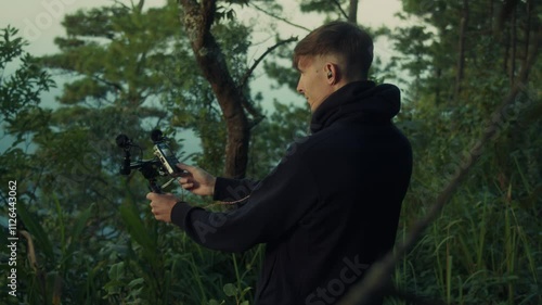 A young man is holding a microphone amidst a serene forest setting, surrounded by nature