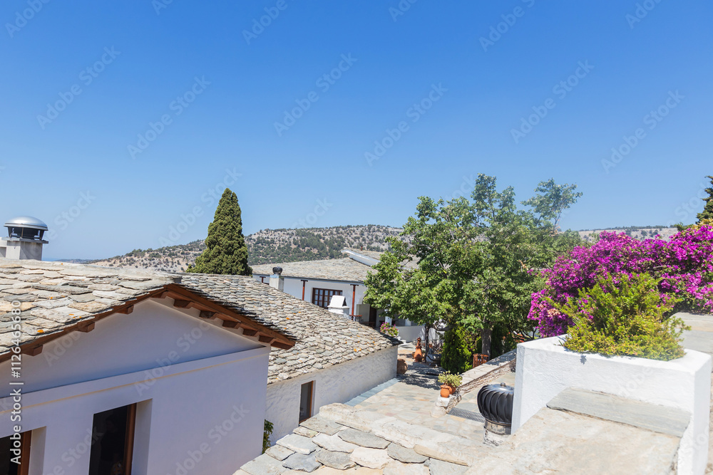 Fototapeta premium Peaceful monastery courtyard featuring blooming bougainvillea and traditional stone roofs in Thassos, Greece.